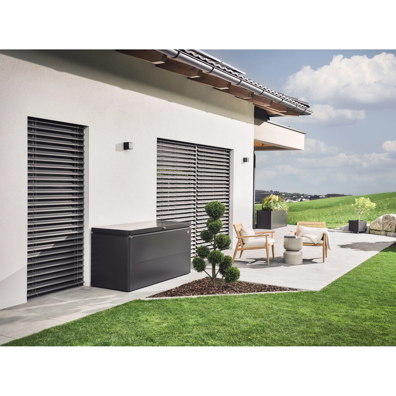 Dunkelgraue Biohort Loungebox 160 auf Terrasse neben Haus. Universalbox für Sitzkissen und Gartenzubehör.