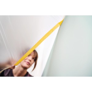 Frau bringt Tesa Abdeckfolie mit Klebeband Easy Cover Perfect+ an Wand an.