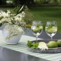 Szene mit Blu Hugo Cocktail-Minze in Vase, Gläsern und Limetten auf einem Tisch im Garten.