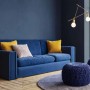 Blaues Sofa mit Kissen und Strickhockern vor blauer Wand.
