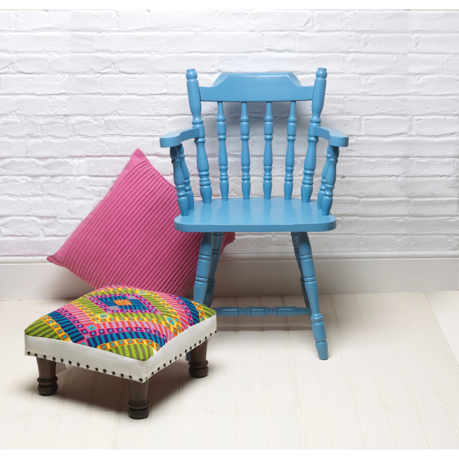 Blauer Stuhl mit Rust-Oleum Kreidefarbe, Kissen und Hocker vor weißer Wand.
