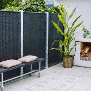 Schwarzer Sichtschutzzaun aus Polyrattan (115x170cm) im Garten mit Bank und Deko.