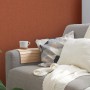 Strukturierte, matte, rote Vliestapete Uni von FSC® an Wand hinter Sofa mit Kissen und Decke.