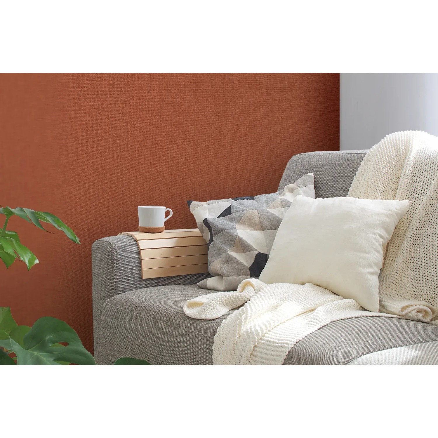 Strukturierte, matte, rote Vliestapete Uni von FSC® an Wand hinter Sofa mit Kissen und Decke.