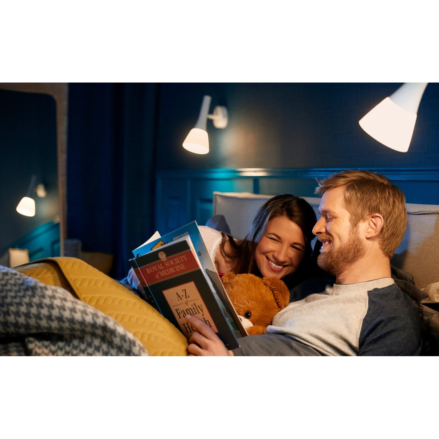 Paar liest im Bett unter Philips Hue White E14 LED Lampen. Smarte Beleuchtung mit Bluetooth.