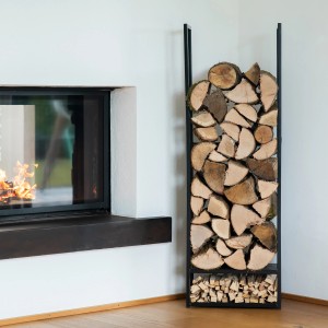 Schwarzes Westmann Kaminholzregal Porthos aus Stahl, gefüllt mit Holzscheiten, neben einem Kamin.