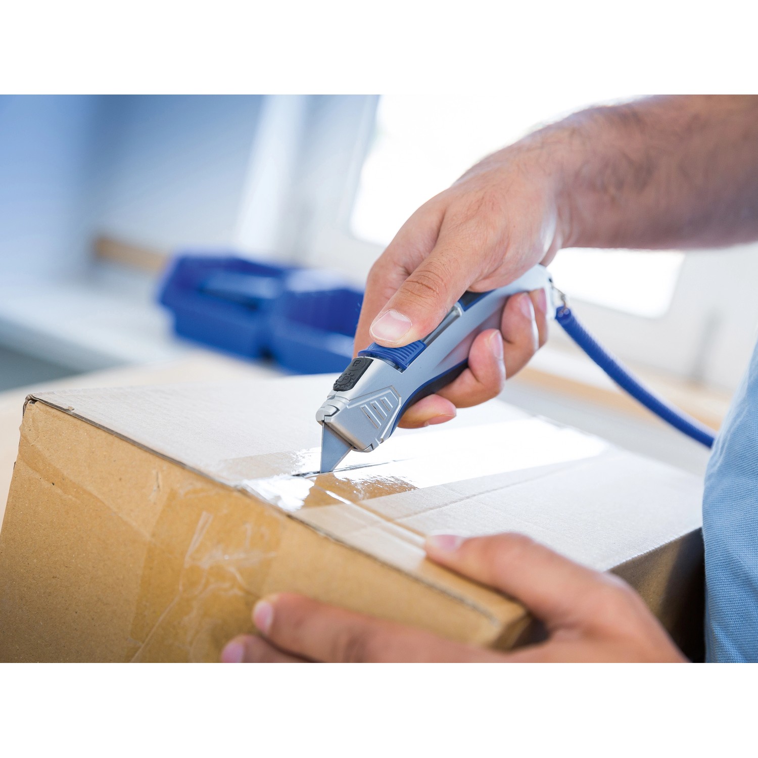 Hand schneidet Karton mit LUX Cuttermesser (grau/blau) mit Tasche.
