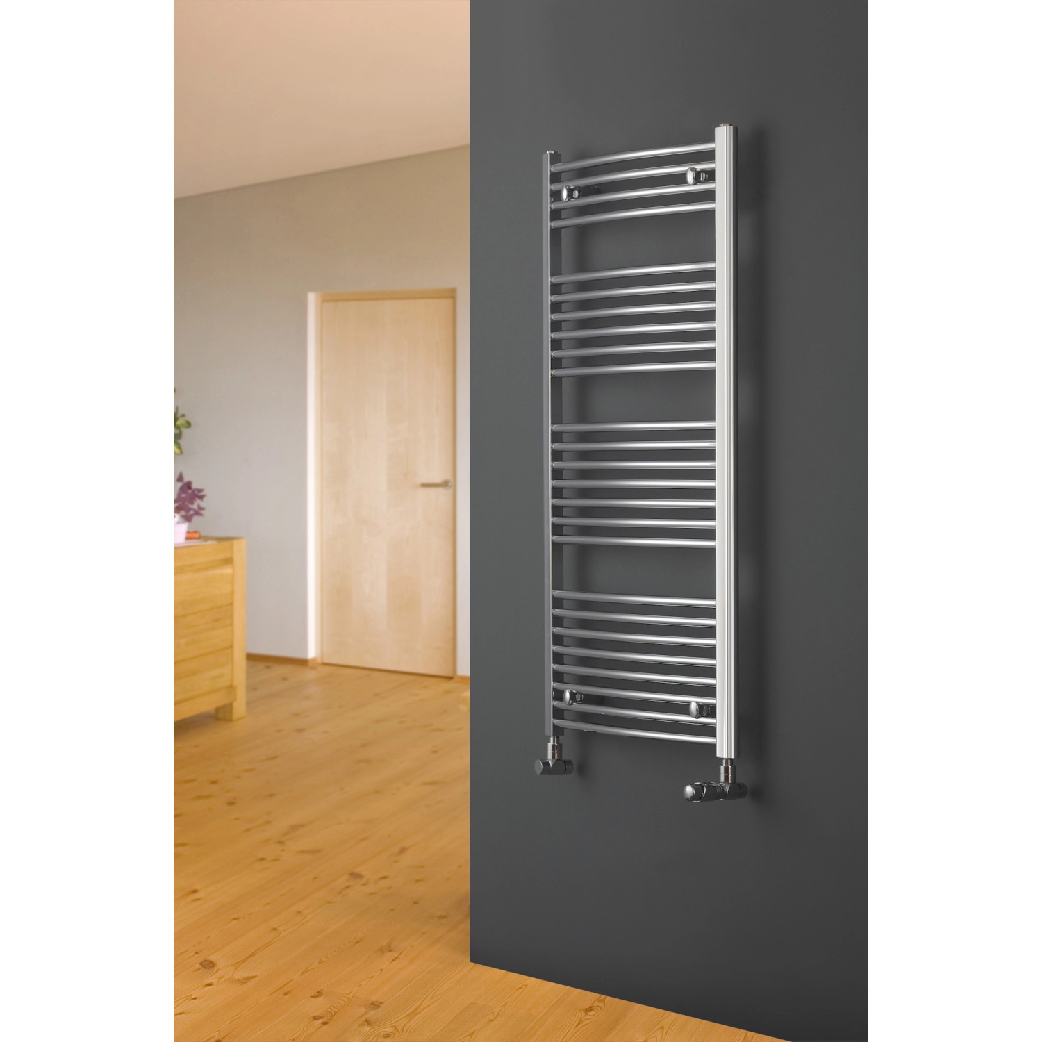 Geschwungener Ximax Badheizkörper C2, Chrom, 1264x600mm, an grauer Wand montiert.