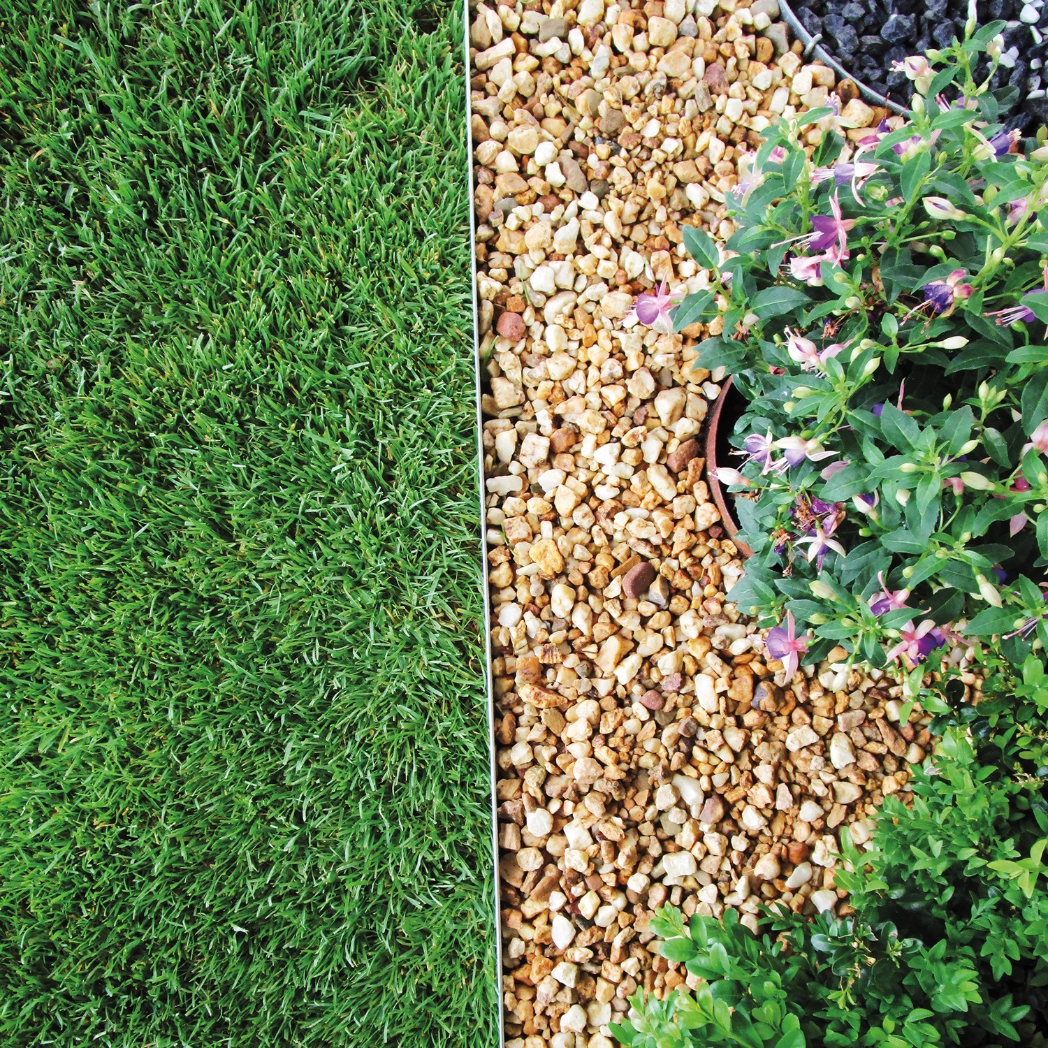 Bellissa Rasenkante aus verzinktem Metall trennt Rasen von Kies und Pflanzen im Garten.