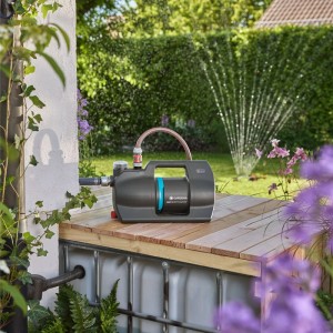Gardena Haus- und Gartenautomat 5000 Silent Comfort auf Holzpodest, Rasensprenger im Hintergrund.