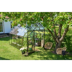 Schwarzes Halls Gewächshaus Qube+ 812 (9,9 m²) im Garten mit Pflanzen und Gartenmöbeln.