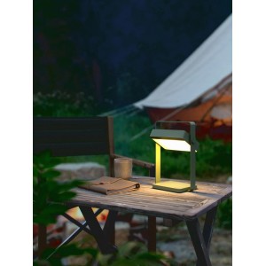Nordlux Saulio Solar-Tischleuchte in Oliv auf Holztisch mit Zelt im Hintergrund.