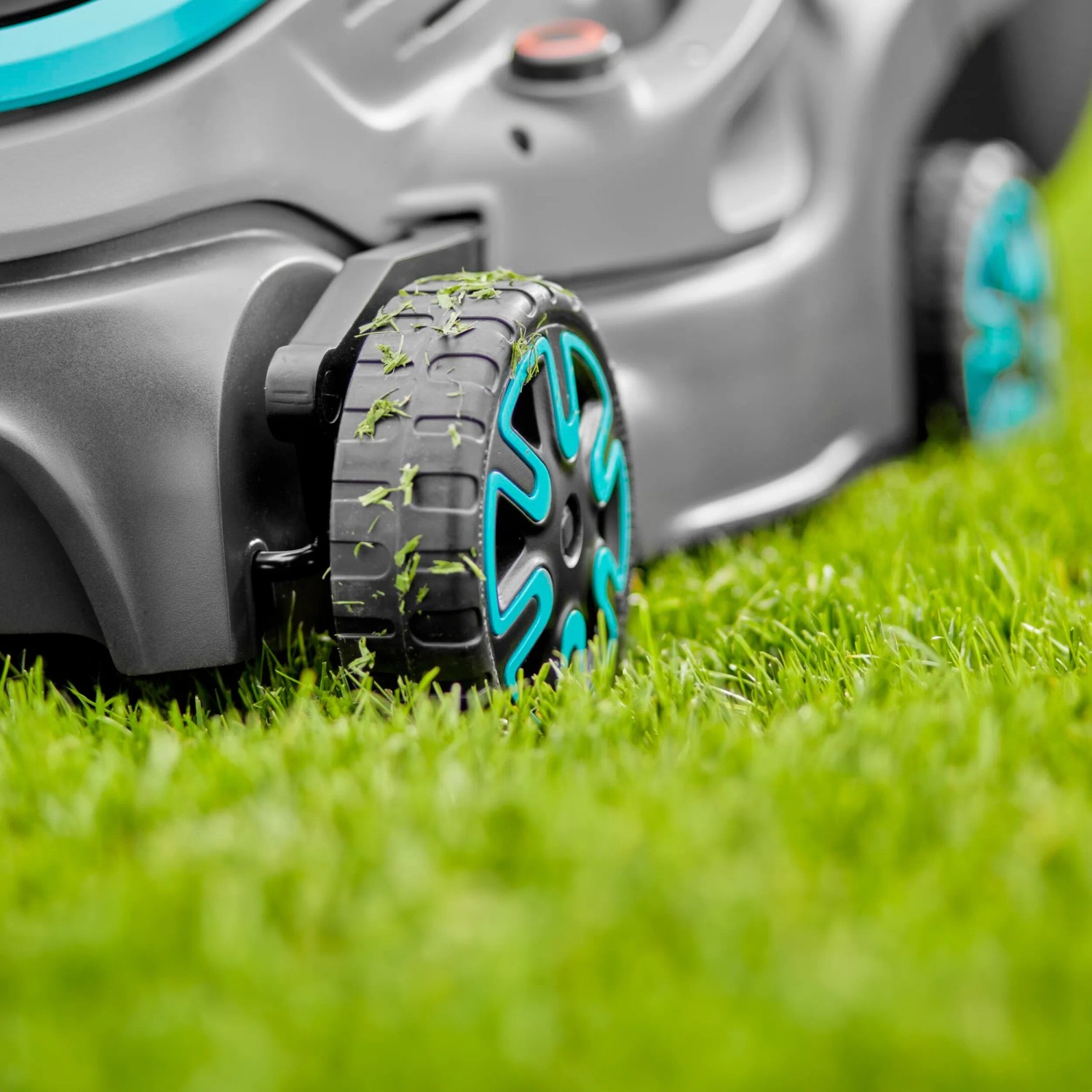 Detailaufnahme: Gardena Akku-Rasenmäher PowerMax 32/18V im Gras. Fokus auf Rad mit Grasresten.