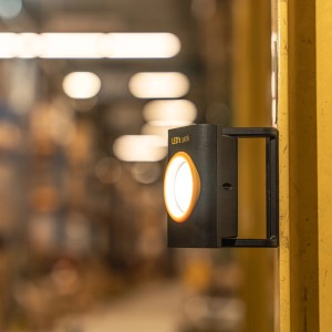 Schwarze LED-Akku-Arbeitsleuchte mit Magnetfuß an gelbem Metallpfosten.