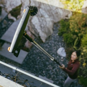 Fiskars Dachrinnenreiniger mit Teleskopstiel im Einsatz, entfernt Laub aus Dachrinne.