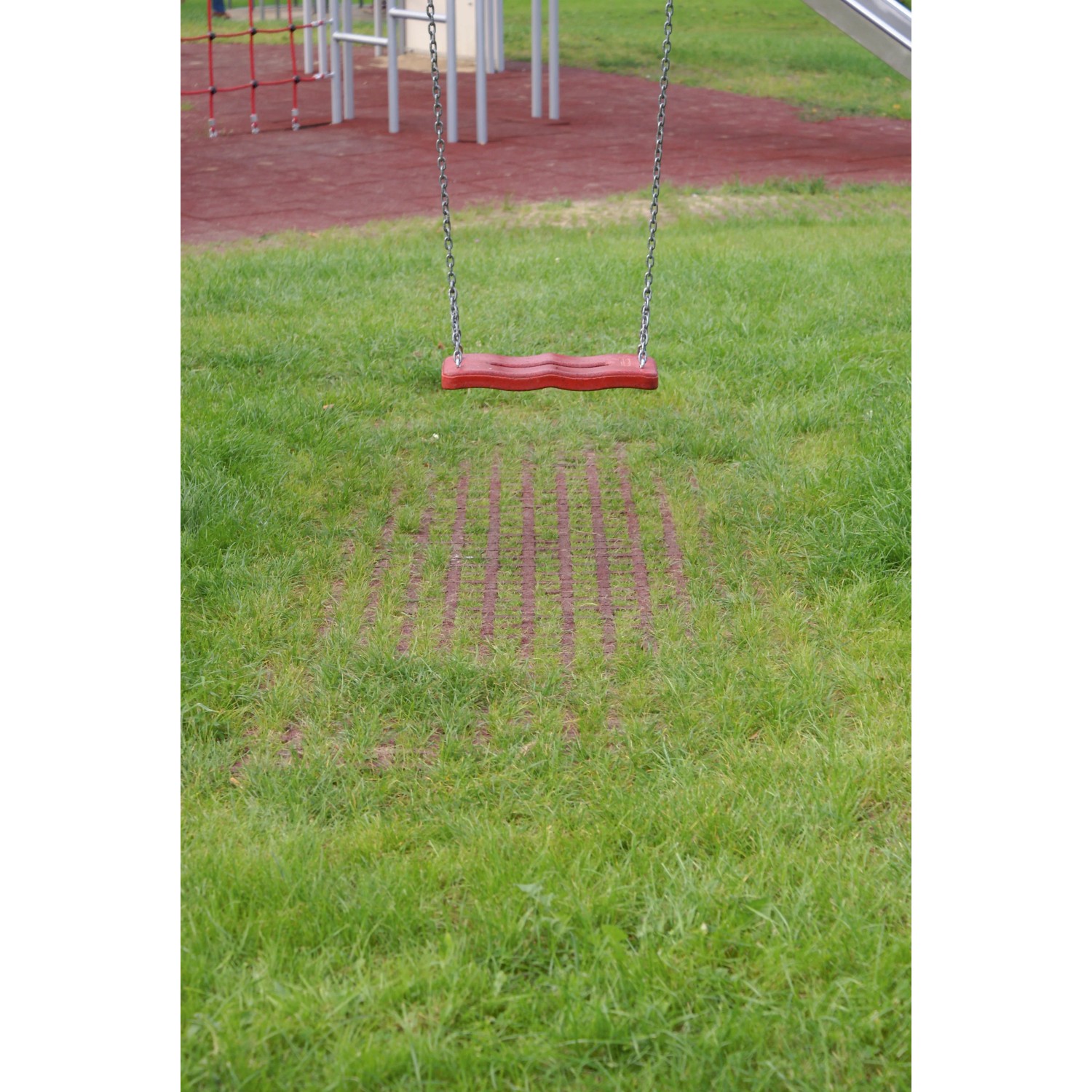 Rote Rasengitter Fallschutzplatte 100x100 cm unter einer Schaukel auf einem Spielplatz.