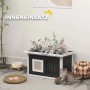 PawHut Katzenhaus grau/weiß aus Tannenholz mit Sisal-Kratzmatte, Blumen auf dem Dach. Katze spielt davor im Innenbereich.