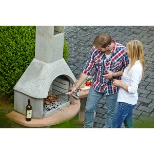 Buschbeck Grillkamin Carmen mit Tisch (grau-terrakotta) beim Grillen im Garten.