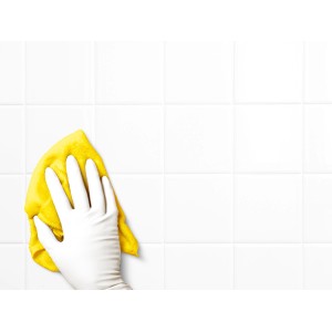 Hand mit weißem, latexfreiem Einmalhandschuh reinigt weiße Fliesen mit gelbem Tuch.