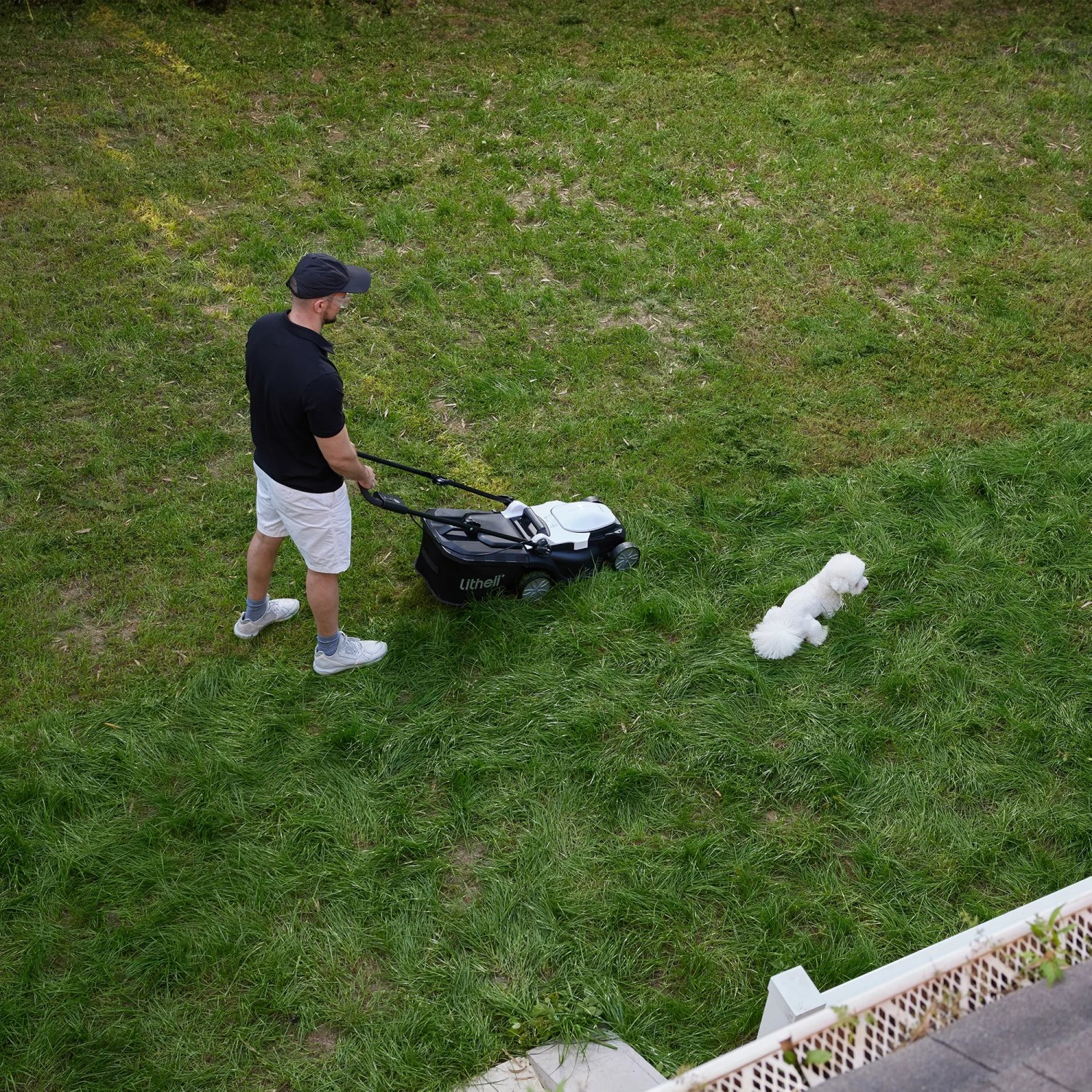 Mann mäht Rasen mit Litheli Akku-Rasenmäher; ein Hund liegt daneben im Gras.
