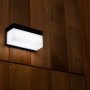 Schwarze Lutec LED Solar Wandleuchte Fran mit Bewegungsmelder an Holzwand.