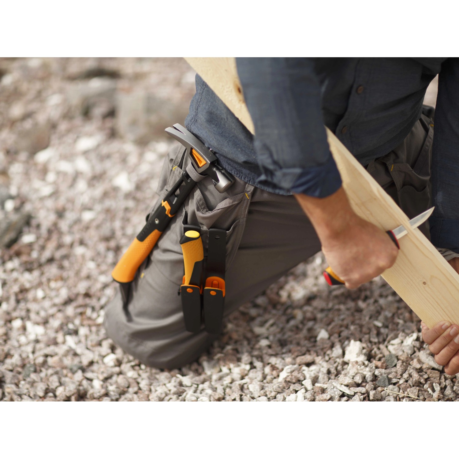 Fiskars Handwerkermesser mit Holster und Messerschärfer im Einsatz beim Bearbeiten eines Holzstücks.