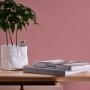 Rosa Vliestapete Uni von A.S. Création im Raum mit Pflanze und Büchern auf einem Tisch.