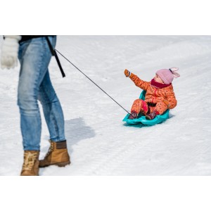 Blauer Babyschlitten mit Lehne und Kind auf Schnee gezogen.