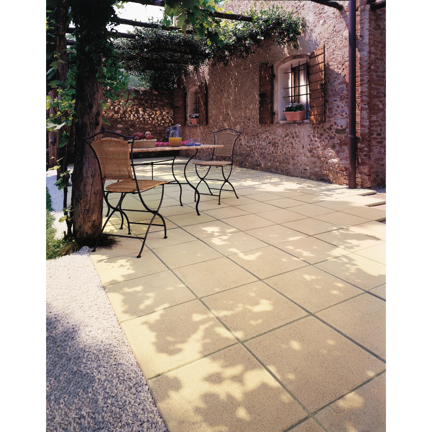 Verlegte Häusler Landhaus Steinplatten in Sandgelb auf einer Terrasse mit Gartenmöbeln.