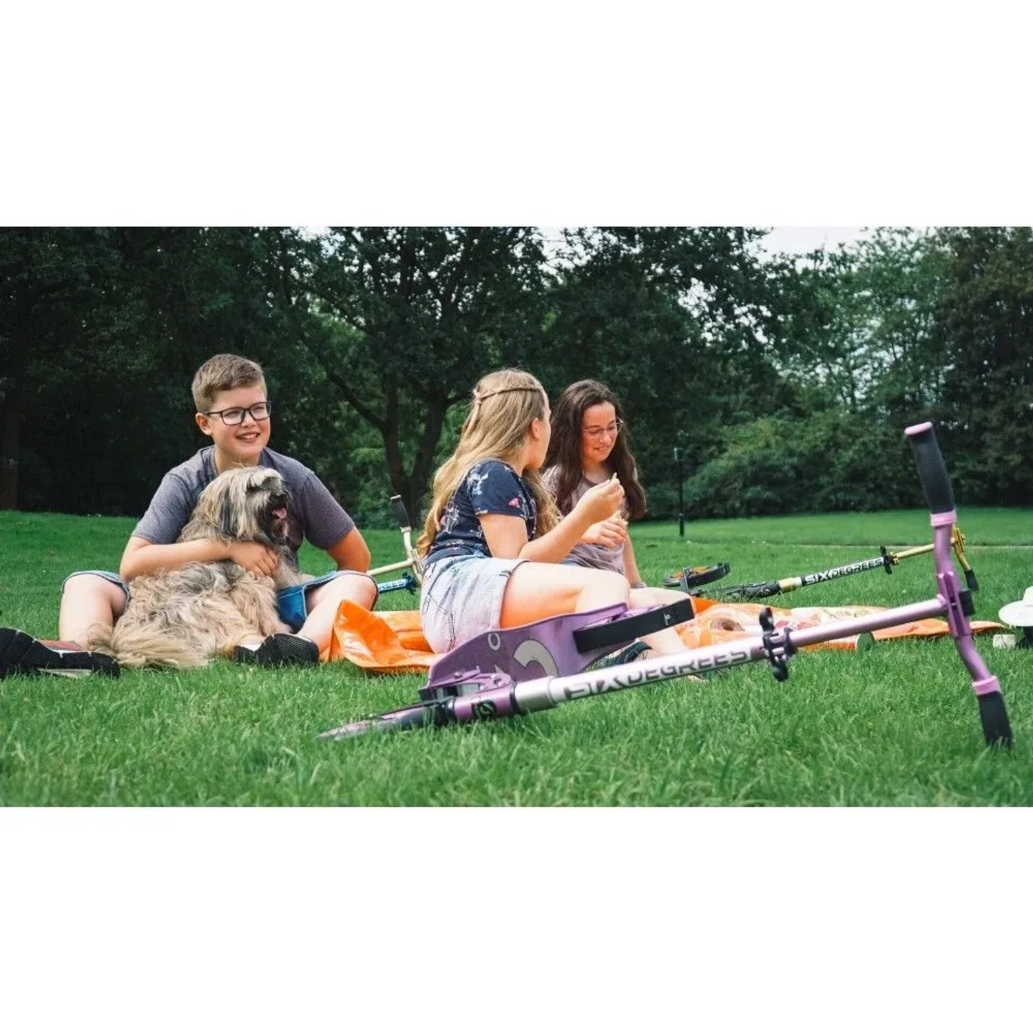 Lila Six Degrees Aluminium Scooter mit Luftbereifung, Klappmechanismus, im Park bei spielenden Kindern.
