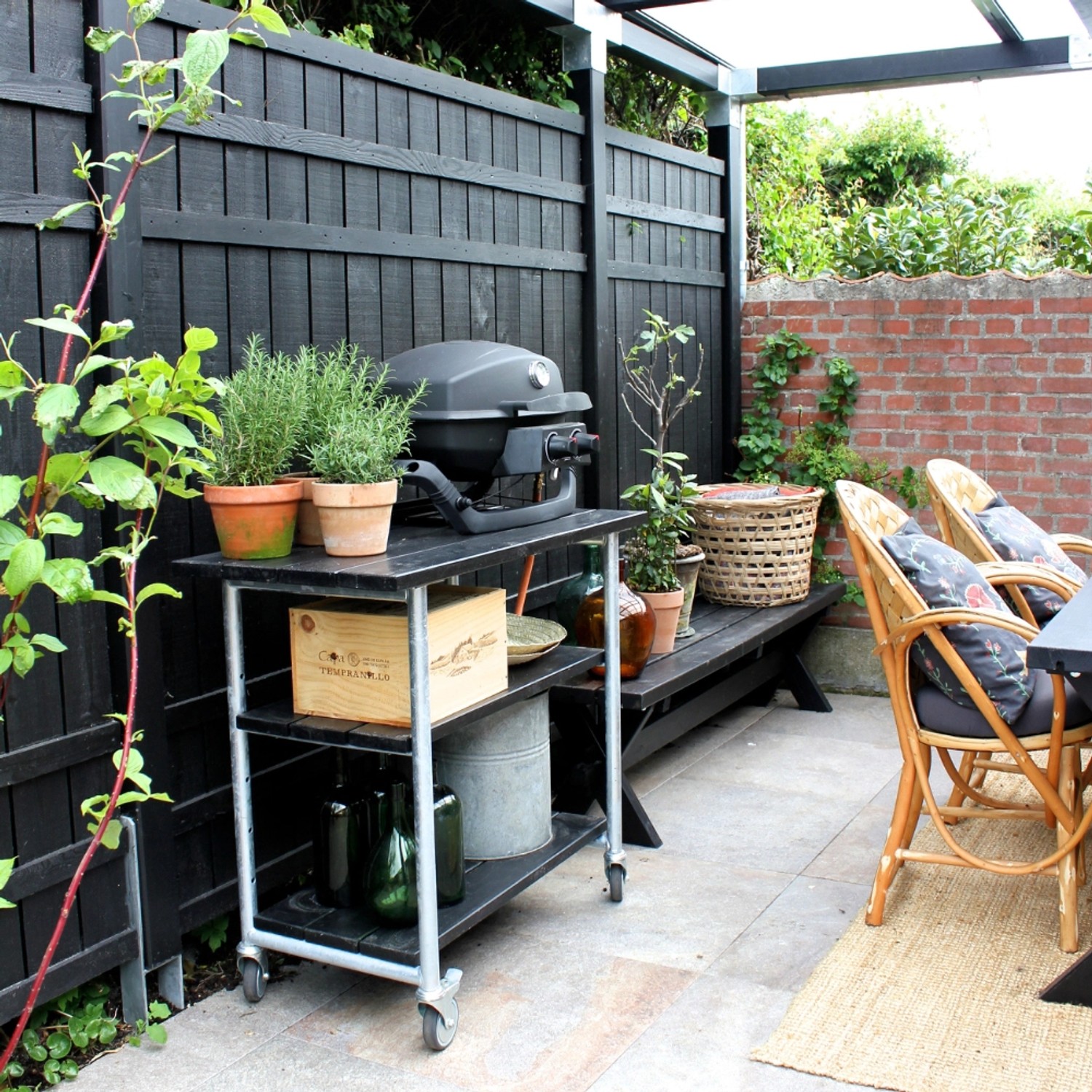 Schwarzer Sichtschutzzaun Rustik Nadelholz (180x180cm) im Gartenambiente mit Grill und Pflanzen.