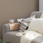 Beige-braune Vliestapete mit leichter Struktur an Wand hinter Sofa mit Kissen und Decke.
