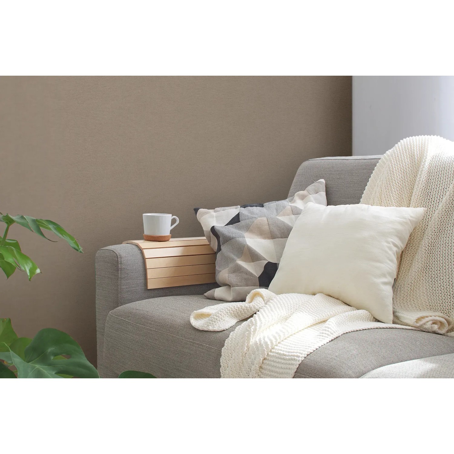 Beige-braune Vliestapete mit leichter Struktur an Wand hinter Sofa mit Kissen und Decke.