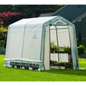 Weißes ShelterLogic Foliengewächshaus 240x180 cm im Garten, bepflanzt mit Blumen und Gemüse.