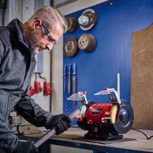 Mann schleift Metall mit Einhell Doppelschleifer TC-BG 150 B. Schleifmaschine mit Funkenschutz.