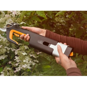 Person schneidet mit Fiskars Akku-Gartenschere L Bypass einen blühenden Strauch. Ergonomische, schwarz-orange Gartenschere für präzise Schnitte.