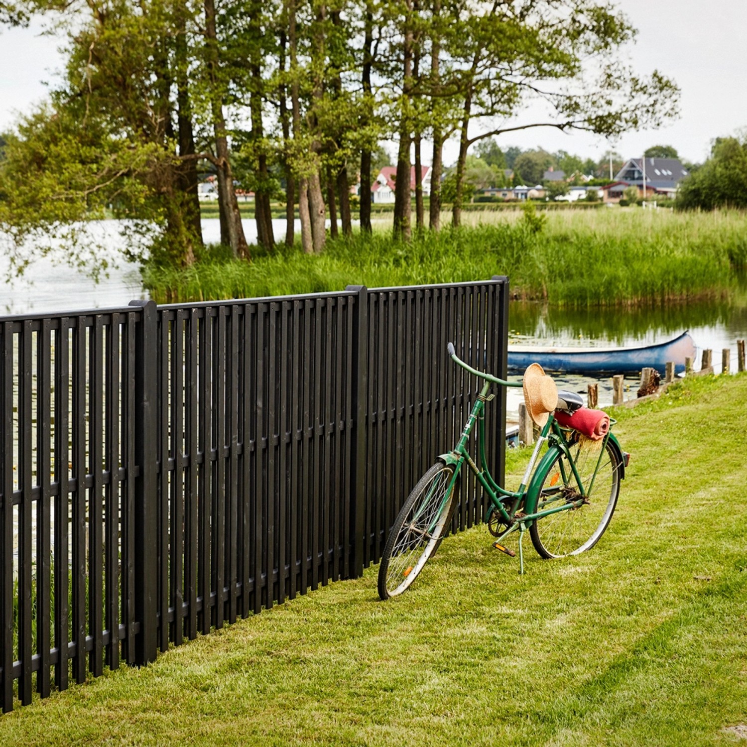 Schwarzer Sichtschutzzaun Nagano aus Nadelholz (180x180cm) mit Fahrrad im Garten am See.