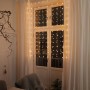 Konstsmide LED-Lichtervorhang mit 120 Sternen, bernsteinfarben, an Fenster mit Vorhängen.