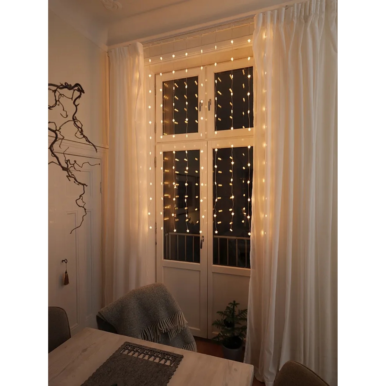 Konstsmide LED-Lichtervorhang mit 120 Sternen, bernsteinfarben, an Fenster mit Vorhängen.