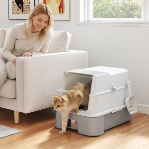Goldene Katze verlässt moderne, geschlossene PawHut Katzentoilette in Grau-Weiß. Frau beobachtet im Wohnzimmer.