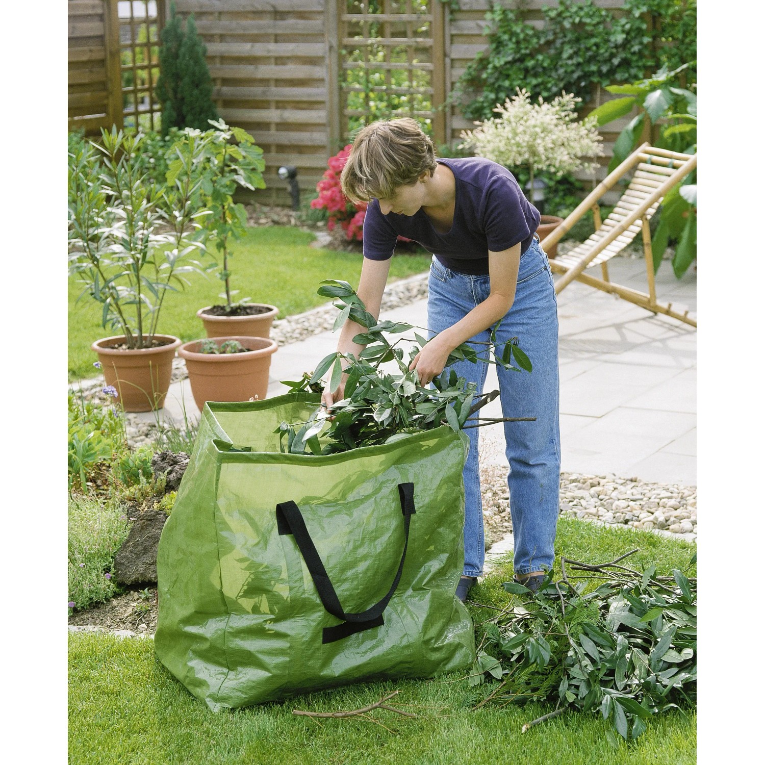 Grüner Gartenabfallsack (245 l) mit Frau beim Befüllen im Garten.
