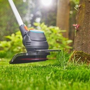 Gardena Akku-Rasentrimmer ComfortCut 23/18 beim Trimmen von Rasenkanten an einem Baum.