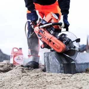 Mann schneidet Stein mit Trennschneider, Aspen 2-Takt Gemisch im Hintergrund.