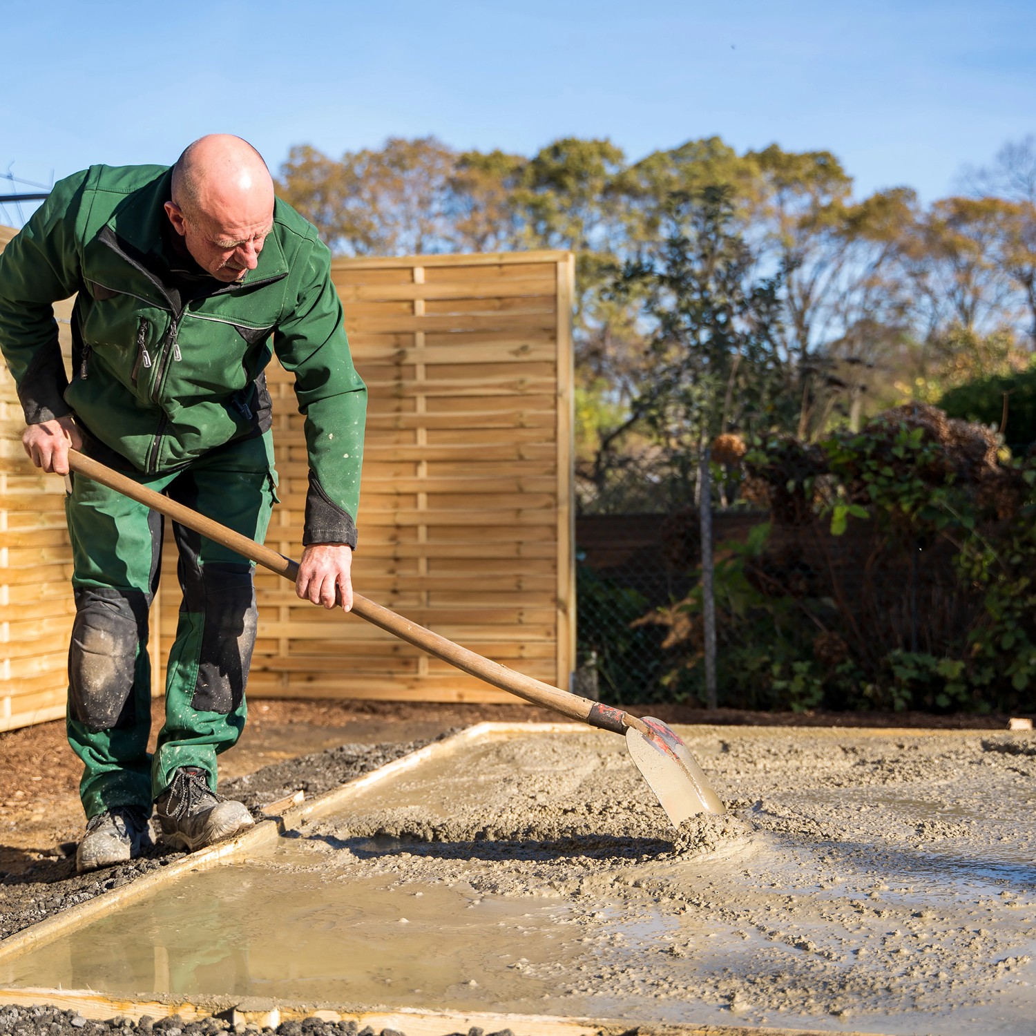 Mann verteilt Pfosten- und Fundamentbeton mit Schaufel für Fundamentbau.