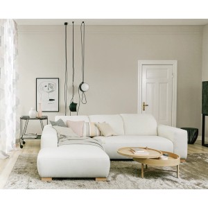 Wohnzimmer mit weißem Ecksofa, Couchtisch und Deko-Elementen vor einer hellen Wand.