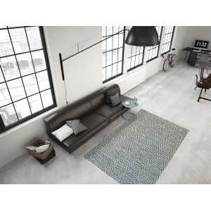 Grauer Wollteppich Melrose 610 (80x150 cm) im Wohnzimmer mit Sofa und großen Fenstern.