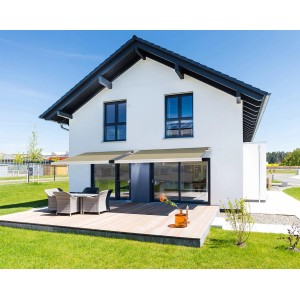 Sandfarbene Home Deluxe LED Vollkassettenmarkise Elos (500x300 cm) am Haus mit Terrasse.
