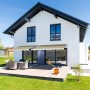 Sandfarbene Home Deluxe LED Vollkassettenmarkise Elos (500x300 cm) am Haus mit Terrasse.
