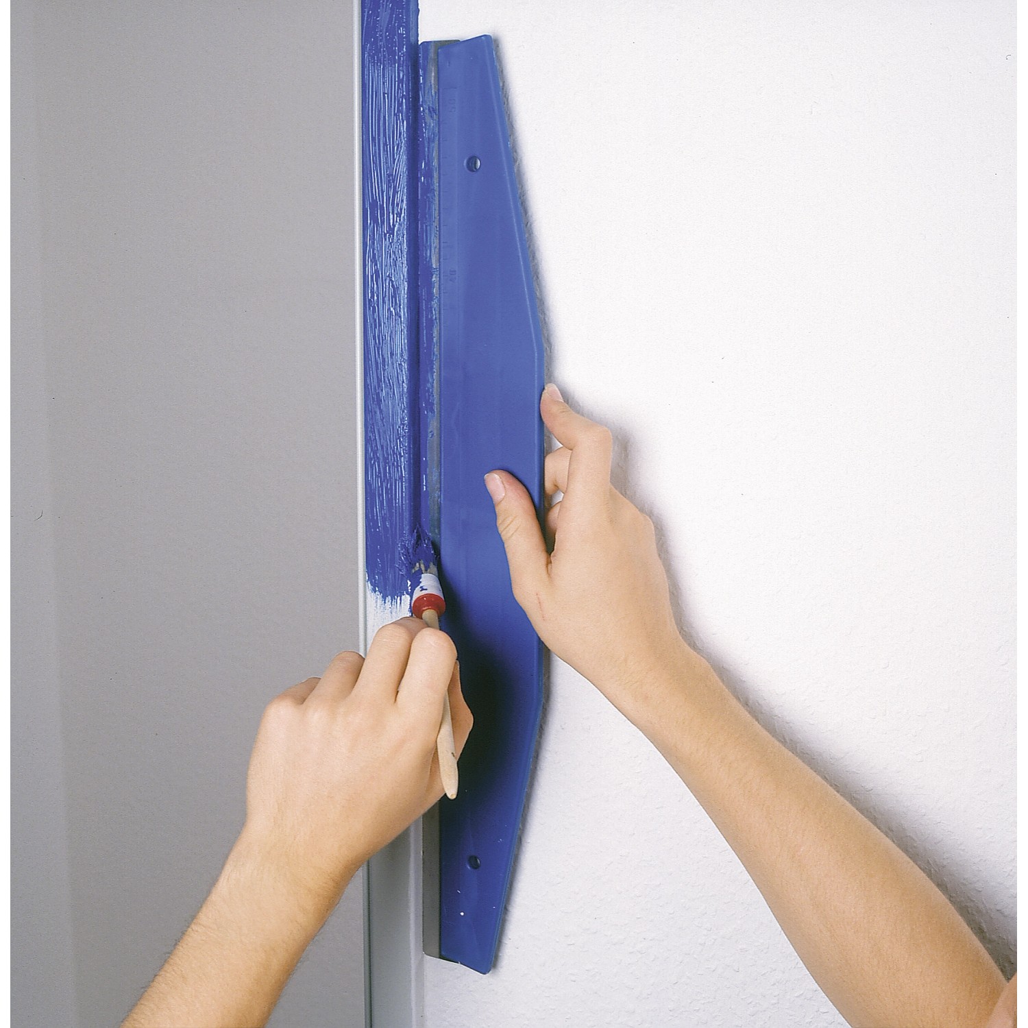 Anwendung des LUX Beschneidelineals 60 cm beim Malen einer Wand mit blauem Farbanstrich.