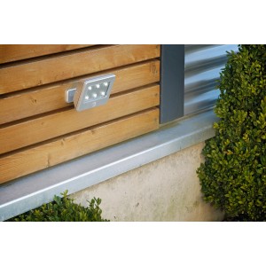 Silberne Briloner LED-Außenwandleuchte Lero mit Bewegungsmelder an einer Holzwand.